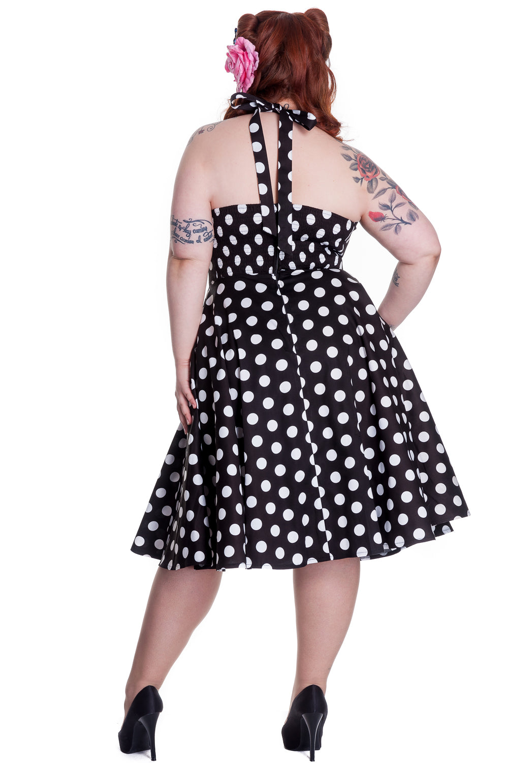 Retro model with tattoos wearing a halter neck 50s style fit and flare polka dot dress