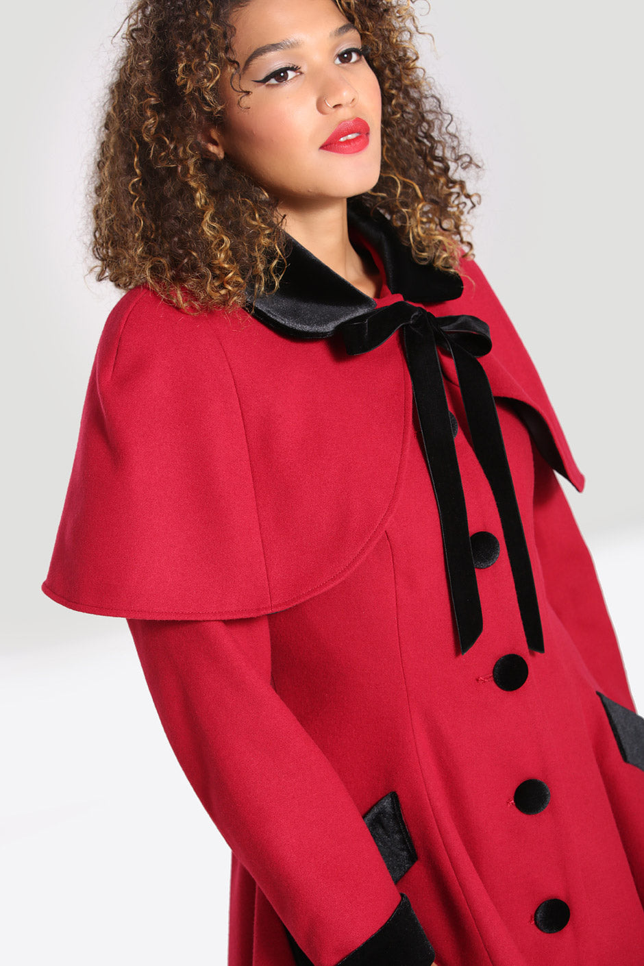 Vintage woman with brown eyes and red lipstick wearing a red coat with a shoulder cape
