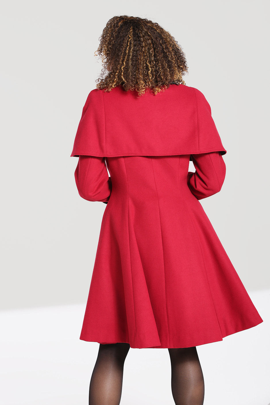 Curly haired woman facing away from the camera wearing a red vintage coat with a short cape around her shoulders