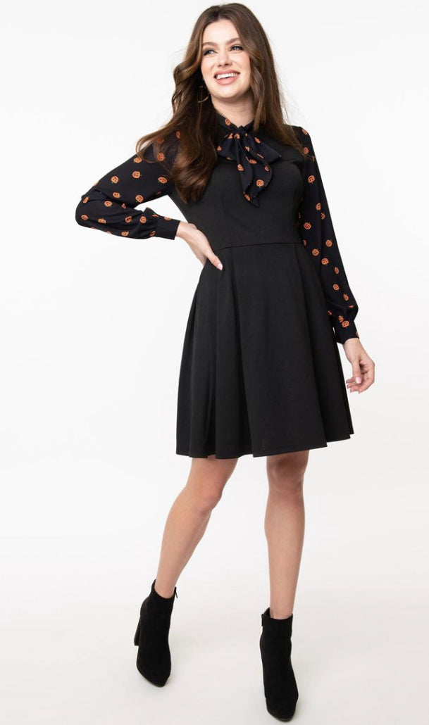 Happy girl laughing with one hand on her hip wearing a pumpkin print black fit and flare dress and black ankle boots