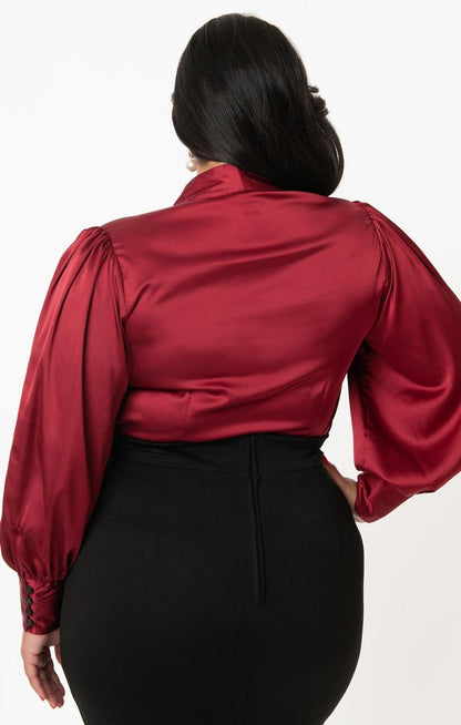 Back view of a dark haired plus size female model wearing a black pencil skirt and a long sleeved burgundy satin blouse