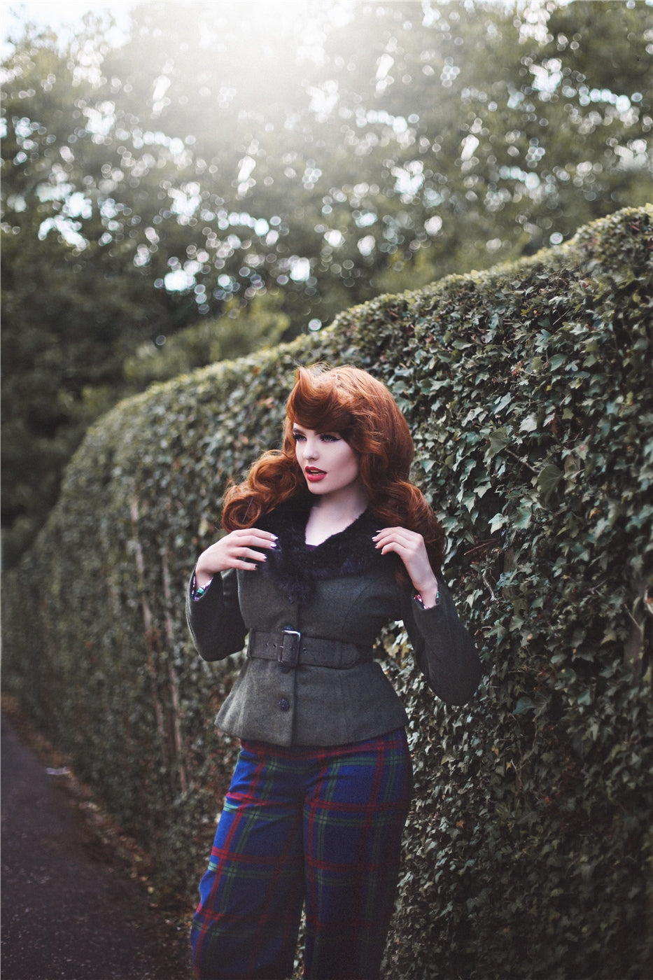 Pretty vintage model with long ginger hair wearing tartan trousers and green belted vintage jacket 