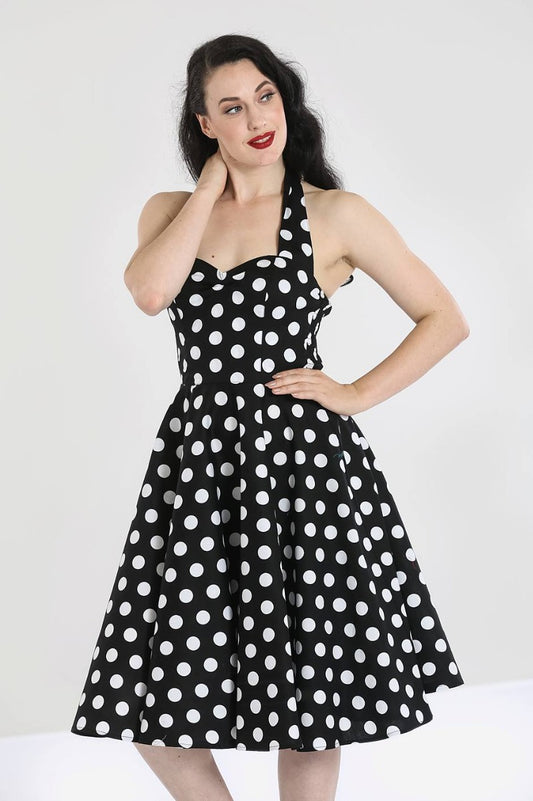 Dark haired smiling pinup vintage model standing with one hand on her hip wearing a black dress with all over white polka dots