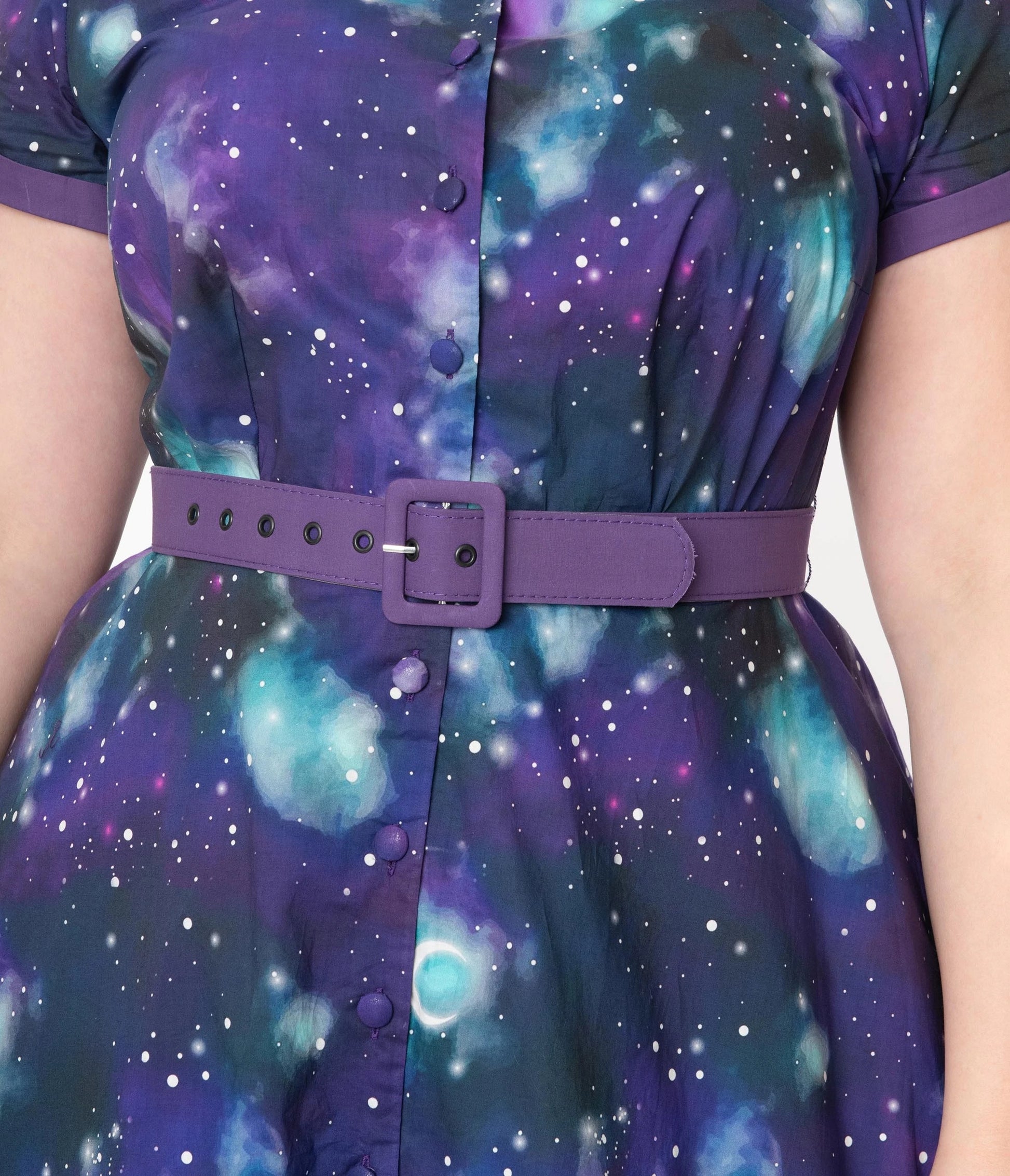 Close up of purple galaxy print dress with white stars and blue nebular patterns. The model is wearing a purple belt and the buttons down the front of the dress are purple fabric
