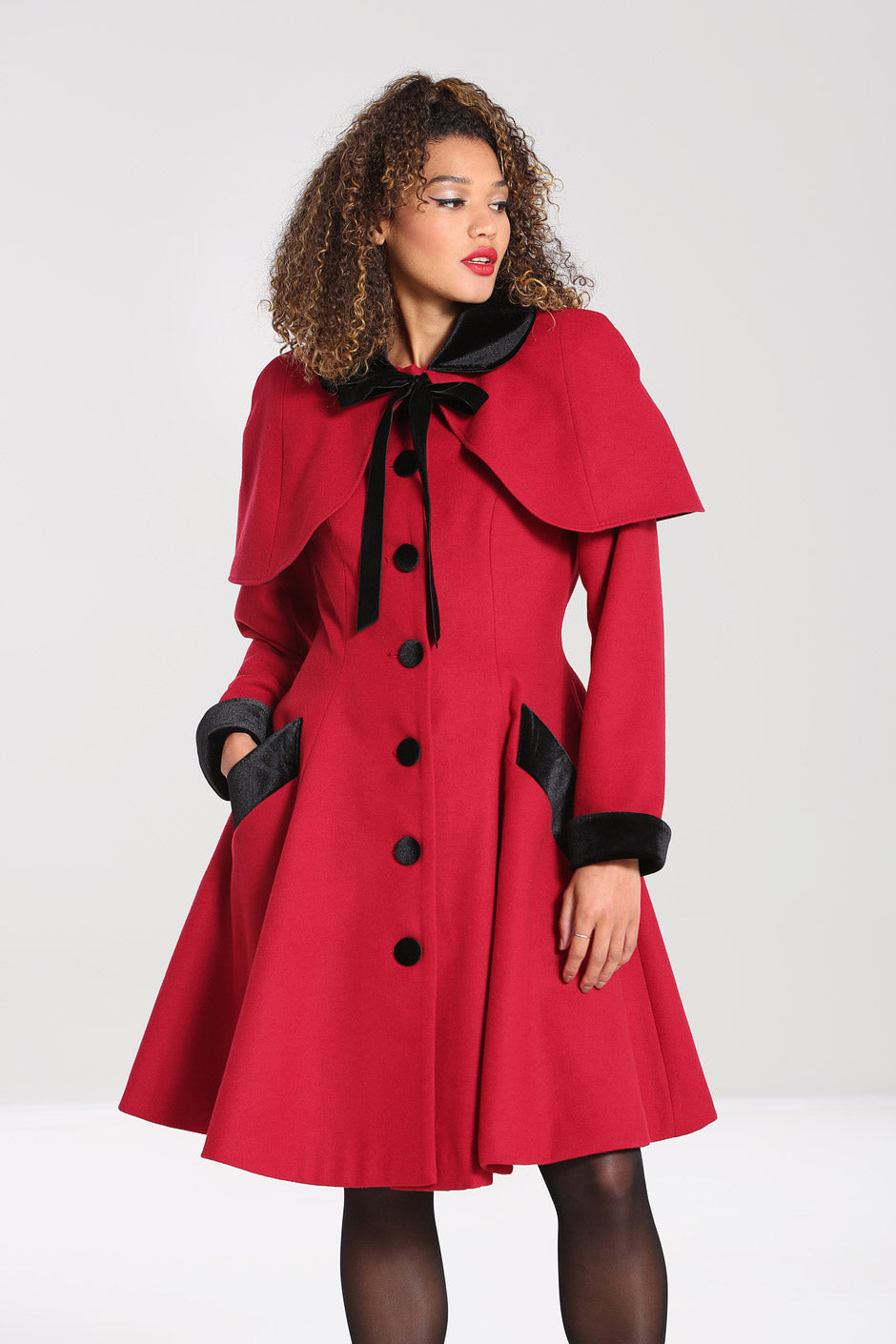 woman wearing vintage makeup with curly hair wearing a red and black 40s style coat 