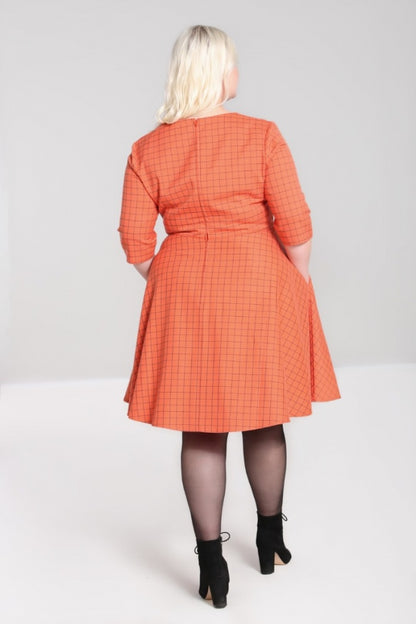 Blonde plus size model facing away from the camera wearing an orange 50s inspired dress which has a zip-closure back, black sheer tights and black ankle boots