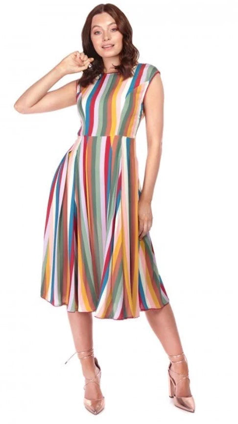 Smiling happy girl with brown wavy hair with one hand raised up to her face, wearing a funky striped dress that drops below the knee