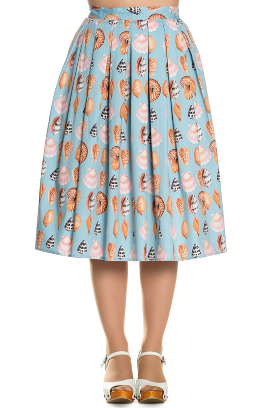 woman standing wearing a light blue pleated skirt with a multicoloured seashells print