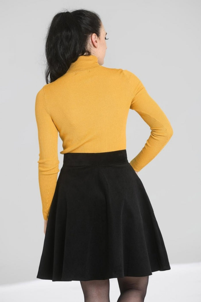 Dark haired woman facing away from the camera wearing the mustard yellow Spiros long sleeved knit top and a black corduroy mini skirt.