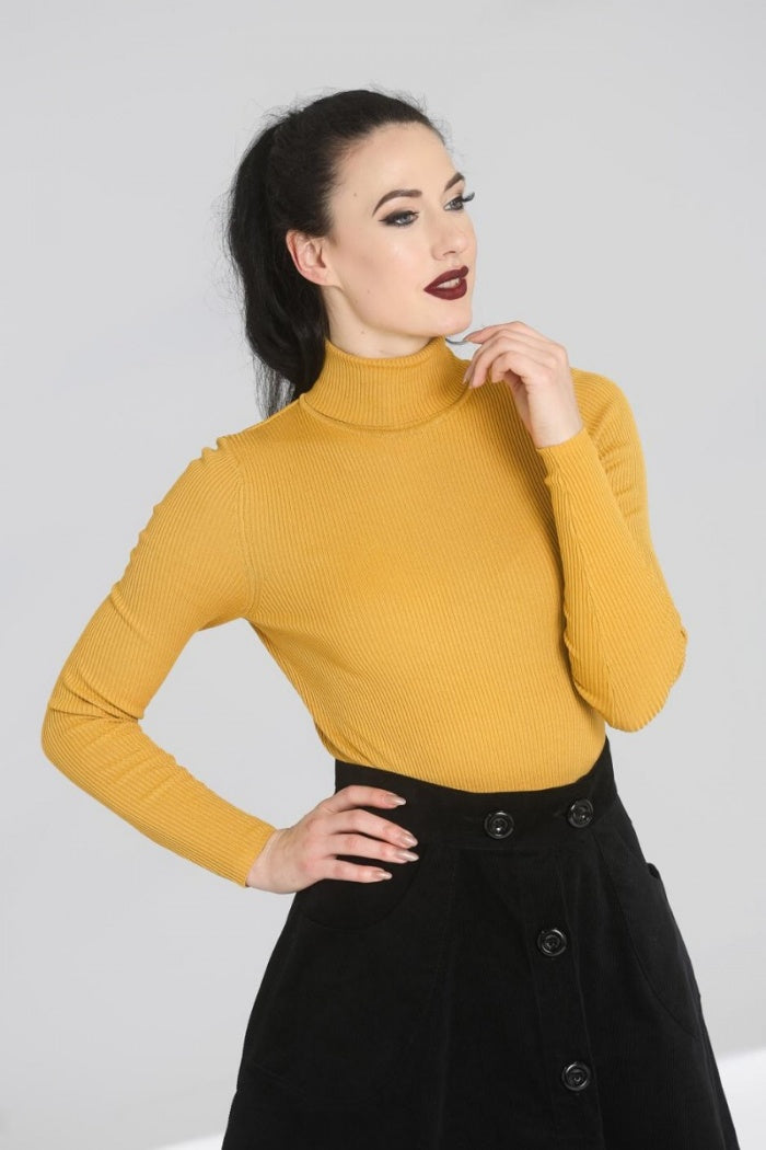 dark haired woman wearing a mustard yellow polo neck top with long sleeves tucked into a black corduroy skirt.